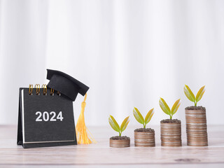 2024 desk calendar with graduation hat and plants growing up on stack of coins. The concept of saving money for education, student loan, scholarship, tuition fees in the future - obrazy, fototapety, plakaty