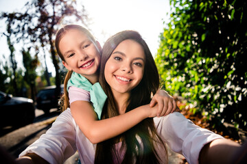 Photo of idyllic lovely sisters cuddle toothy smile take selfie record video sunny weather walk park outdoors