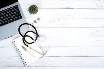 Medical technology and healthy concept on modern white table desk background with stethoscope and laptop computer, blank notepad and supplies, Top view with copy space