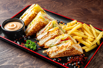 Delicious club sandwiches with fries and sauce on a stylish black plate, garnished for a gourmet meal