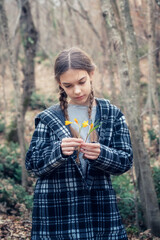 Beautiful caucasian girl with braids holding a bouquet of yellow crocuses at the background of a spring forest. - 752346821