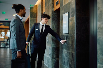 Happy hotel attendant and black businessman waiting for elevator in lobby, © Drazen