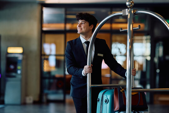 Happy hotel attendant pushing luggage cart through the hallway.