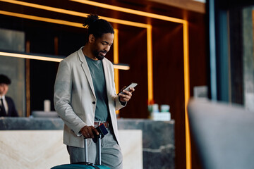 Happy black man using cell phone in hotel lobby.