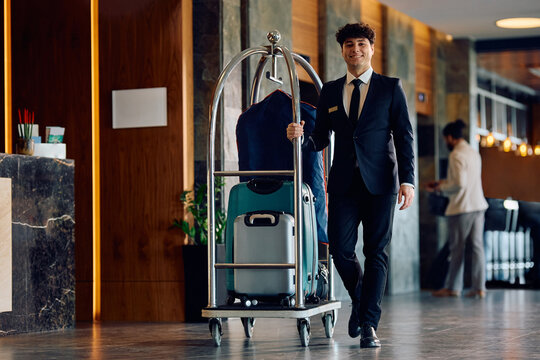Happy hotel attendant luggage cart through lobby and looking at camera.