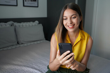 Attractive Brazilian girl using mobile phone sitting in her room at home