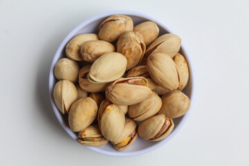 Salted pistachio on the small white bowl, isolated on white background, flat lay or top view