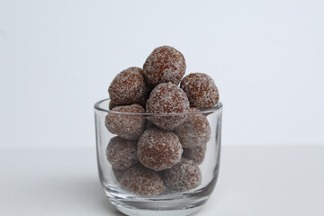 Tamarind candies in small glass. Sweet and sour candy made from tamarind paste and coated by sugar. Isolated on white background