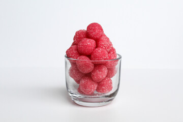 Soursop candy, in pink color and ball shaped, coated by sugar. In transparent glass bowl. Isolated on white background