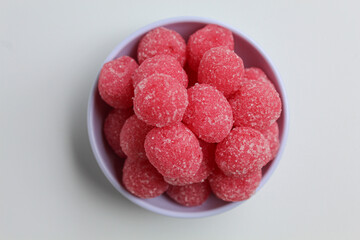 Soursop candy, in pink color and ball shaped, coated by sugar. Isolated on white background, in a small white bowl, flat lay or top view