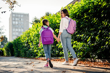 Obraz premium Full body rear behind photo of two charming sisters carry rucksack hold arms walk chatting sunshine park outside
