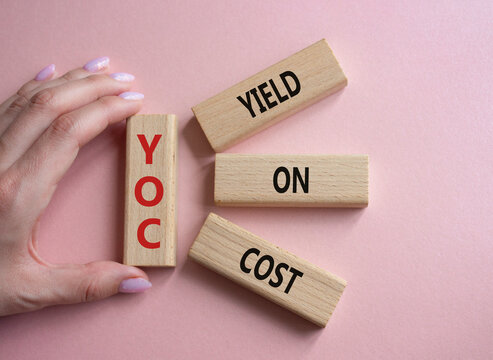 YOC - Yield on Cost. Wooden cubes with word YOC. Businessman hand. Beautiful pink background. Business and YOC concept. Copy space.