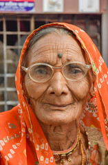 Elderly woman with googles, wrinkles and orange sari looking to camera confident