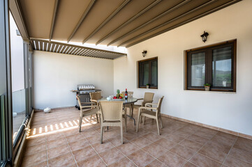 delightful covered terrace in front of house, featuring beautifully set table with chairs and BBQ, creating inviting outdoor area for al fresco gatherings, relaxation.
