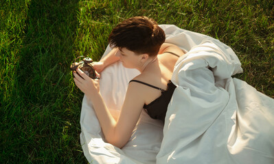 A girl wrapped in a blanket lies on green grass next to an alarm clock, promoting healthy sleep...