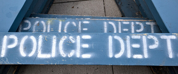 police dept (department) sign on blue wooden barricade laid on cement pavement sidewalk (painted...