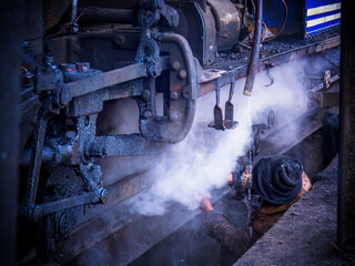 A railway mechanic working under a steam locomotive