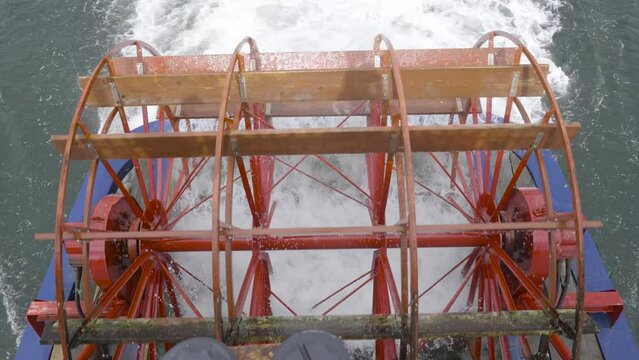 A 4k slow-motion video with a top-down view of a red paddle wheel on the back of a paddle boat.