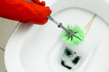 Hands in red gloves cleaning WC, toilet, using brush. Limescale. Hard water. Cleaning toilet bowl with limescale using detergent. Cleaning service concept