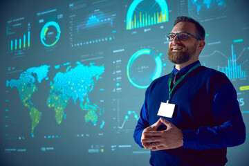 Smiling businessman with glasses presenting analytical data visualizations on large screen. Morning...