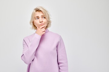 Pensive young woman in a purple sweater, hand on chin, looking thoughtful on a light background.