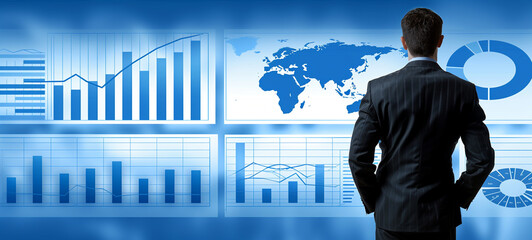 A businessman gazes at a wall-sized display of global data analytics and business metrics