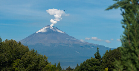 Majesty in Repose: A snow-capped volcano whispers smoke into the blue expanse as nature's silent...