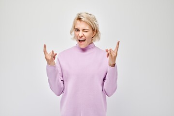 Excited woman in a pink sweater making rock and roll hand gesture, isolated on a white background.