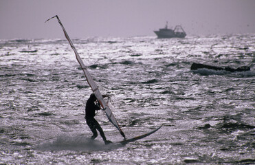 Windsurfing on the Alghero coast, a fishermen boat in the background. Sardinia. Italy