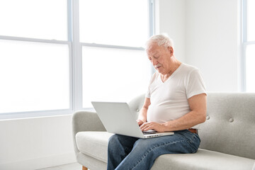 senior men using a laptop while sitting on couch at home