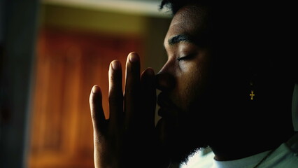 Profile close-up face of a young black man PRAYING to GOD. Meditative African American person with...