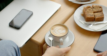 People having breakfast at a cafe, enjoying a cup of coffee paired with a slice of delicious banana bread. Classic morning staples like freshly brewed coffee and flaky pastries. Phone on the table.