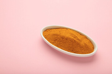 Turmeric (Curcuma) powder on white plate on pink background