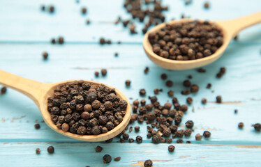 Black pepper corns in wooden spoon on blue wooden background