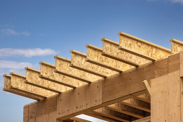 Engineered wood joists or rafters forming the roof of a house under construction