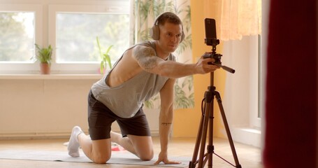 Preparing for a home online workout session, a man sets up his smartphone on a tripod to connect with the trainer. Virtual training sessions from the comfort of his own home. 