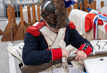 Golfe-Juan, Vallauris, France - 02 March 2024: Historical reenactment of events. Landing on the shore in 1815 of Emperor Napoleon I Bonaparte. A man in a military uniform is cleaning a rifle.