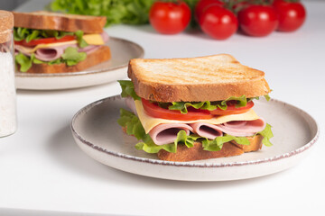 Close-up of two sandwiches with bacon, salami, prosciutto and fresh vegetables on rustic wooden cutting board. Club sandwich concept