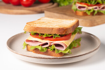 Close-up of two sandwiches with bacon, salami, prosciutto and fresh vegetables on rustic wooden cutting board. Club sandwich concept