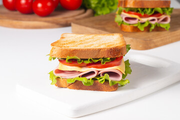 Close-up of two sandwiches with bacon, salami, prosciutto and fresh vegetables on rustic wooden cutting board. Club sandwich concept - 752430864