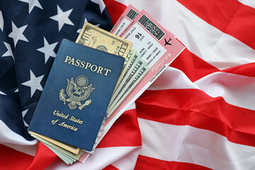 Blue United States of America passport with money and airline tickets on US flag background close up. Tourism and travel concept
