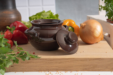A baking pot on the kitchen table among vegetables and herbs