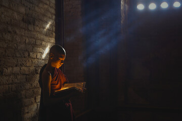 Young novice monk praying with candles in front of buddha statue inside old pagoda, Bagan Myanmar