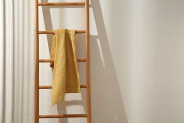 Yellow towel hanging on wooden ladder indoors. Space for text © New Africa