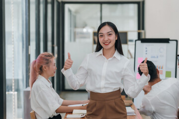 Confident young professional asian businesswoman giving thumbs up in a meeting. Positive feedback and agreement concept.