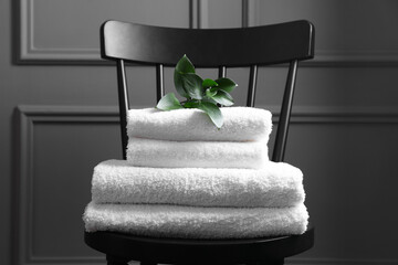 Stacked soft towels and green leaves on black chair indoors
