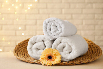 Rolled terry towels and flower on white table near brick wall indoors, space for text
