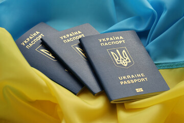 Three Ukrainian biometrical passports on folded waving flag of Ukraine country close up