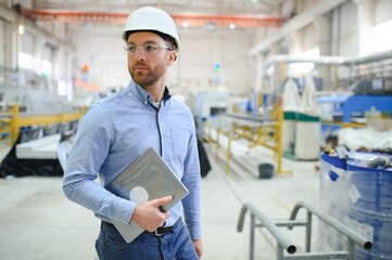Engineer in hardhat is using a laptop in a heavy industry factory