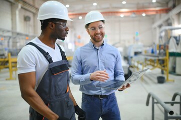 Two workers in production plant as team discussing, industrial scene in background